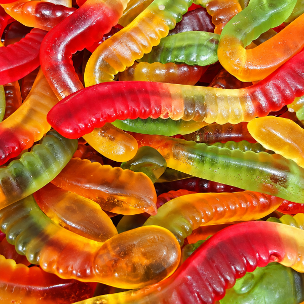 A close-up pile of gummy worms candy, showing translucent pieces in red, orange, yellow, and green.